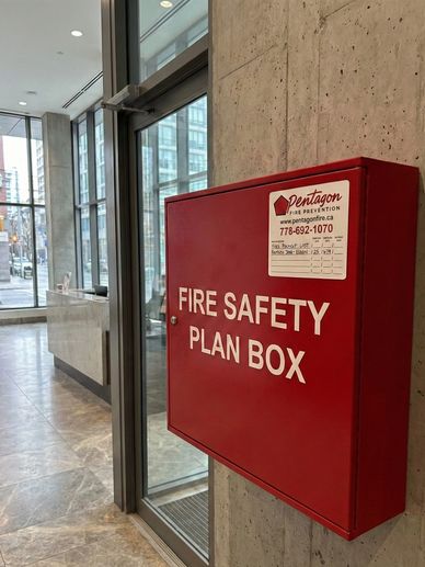 Red fire safety plan box mounted on a concrete wall in a modern building lobby.