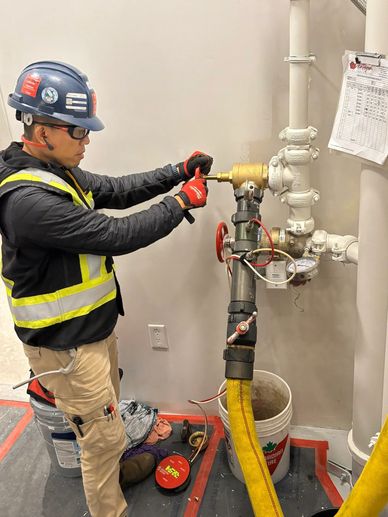 Worker in safety gear fixing a pipe connection indoors.