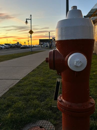 Red and white fire hydrant on a grassy sidewalk at sunset.