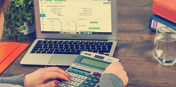 Person using a calculator and laptop for financial calculations at a wooden desk.