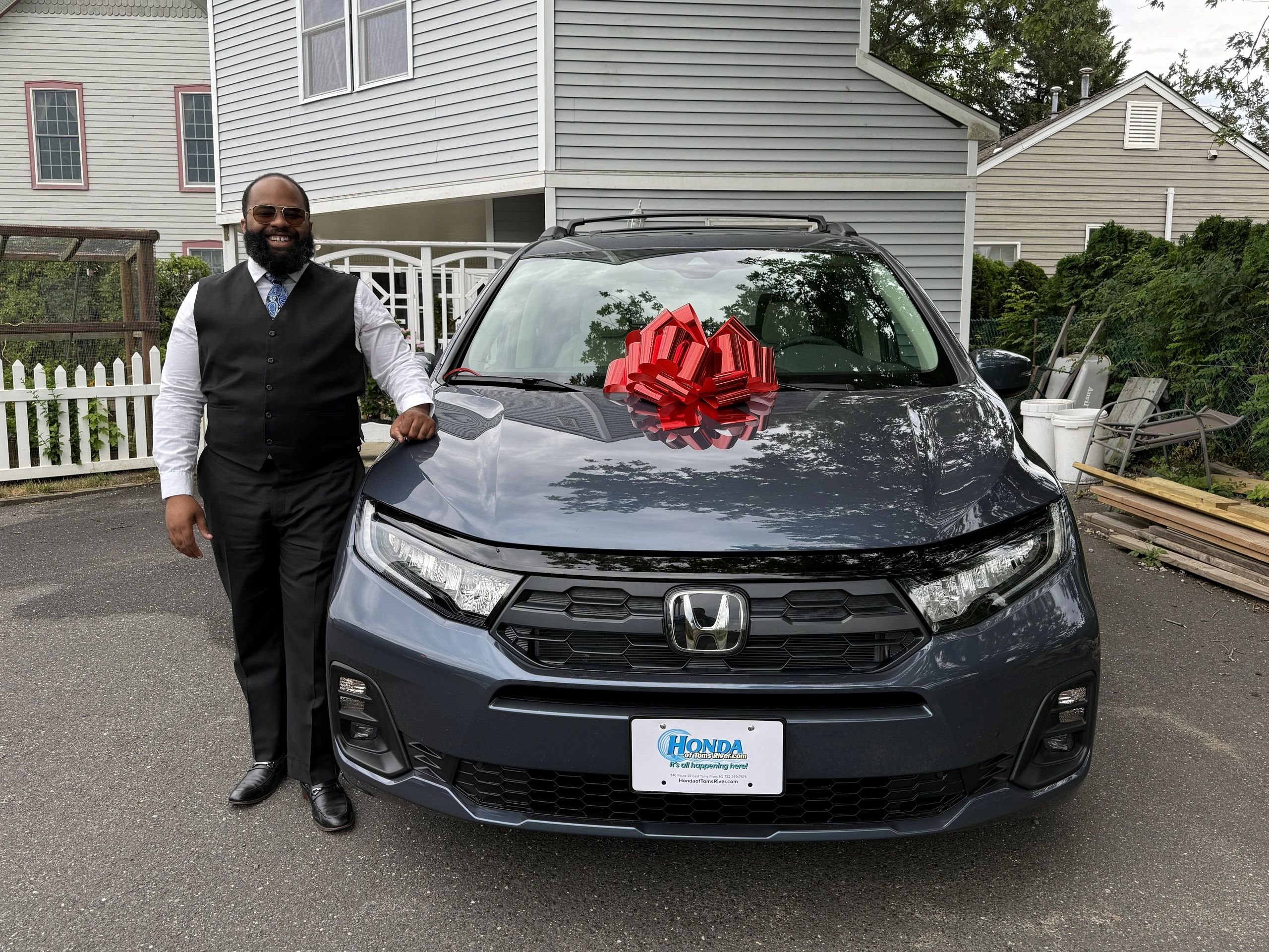 Man smiling next to a new Honda car with a red bow on the hood.