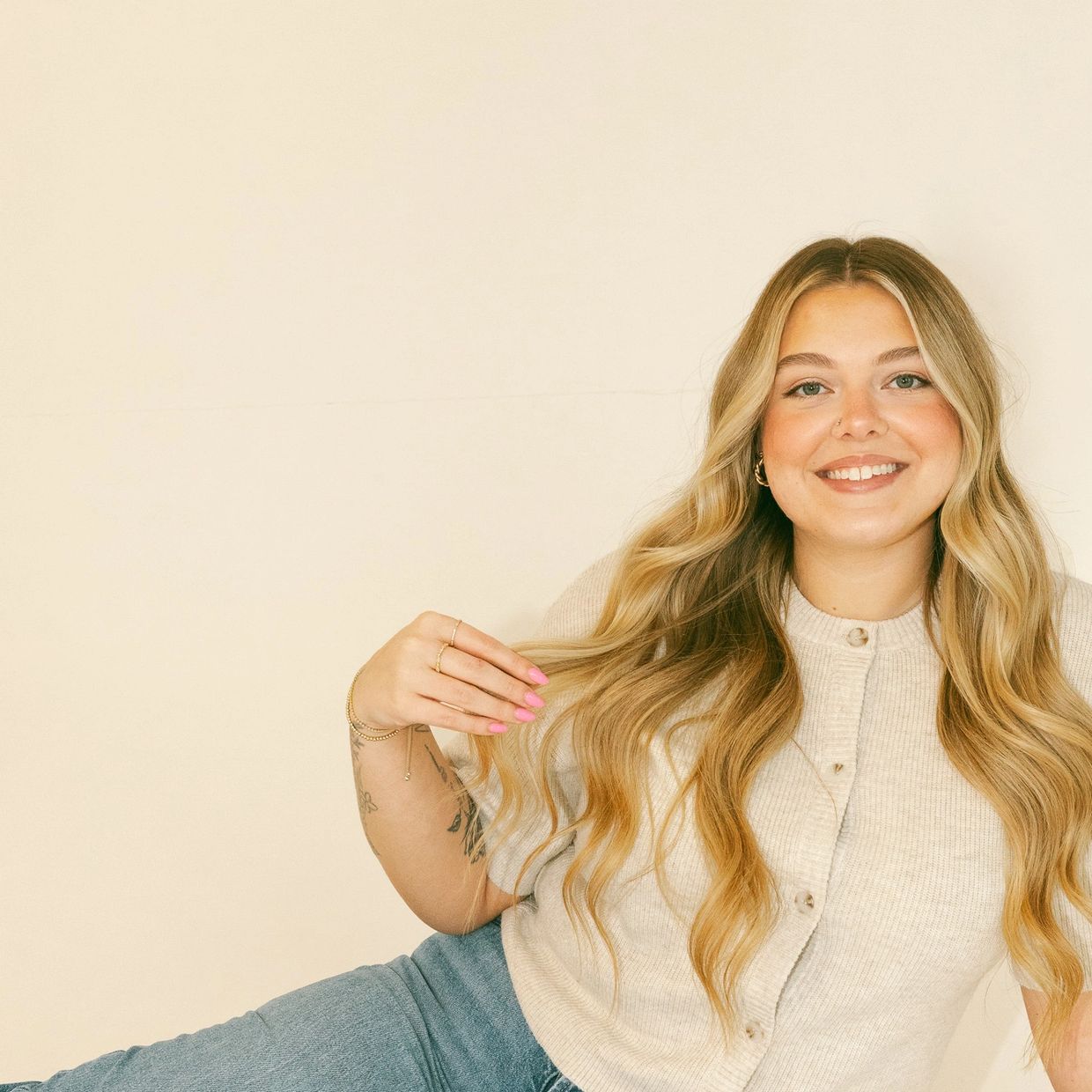 Smiling woman with long wavy blonde hair wearing a beige buttoned top.