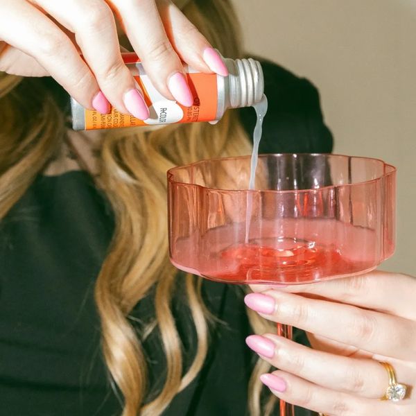 Person pouring liquid from a small bottle into a pink glass dish.