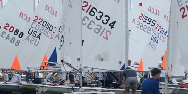 Sailboats with numbered sails preparing for a race on a cloudy day.