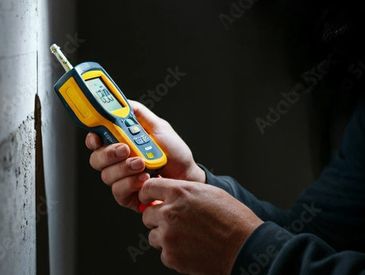 Person holding a gas detector near a wall.