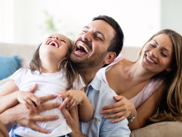 A happy family laughing together on a couch in a cozy living room.