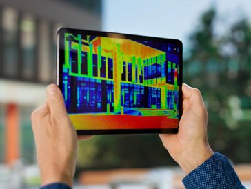 Person holding a tablet showing thermal imaging of a building.