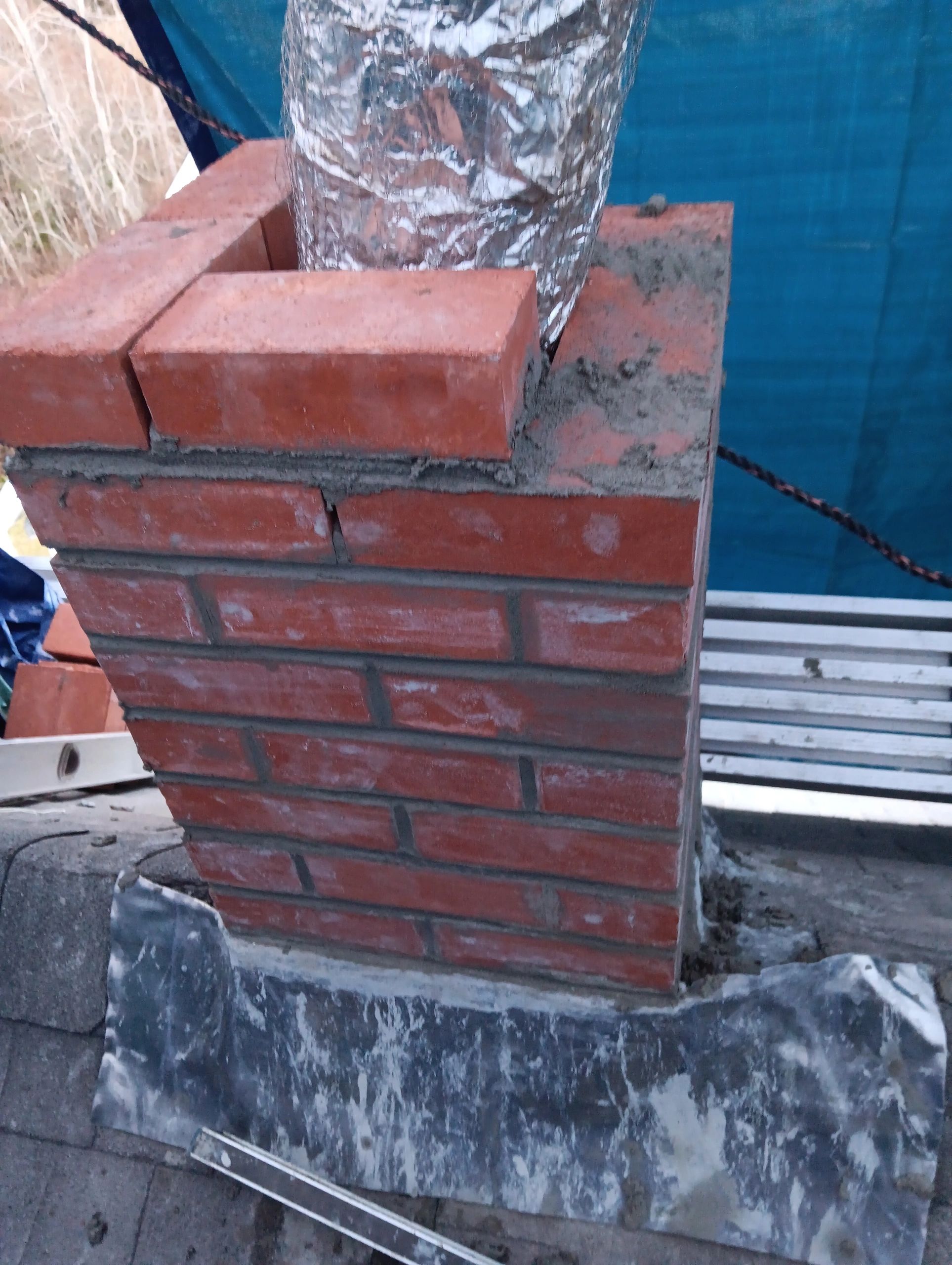 Partially built brick chimney with metal duct and mortar.