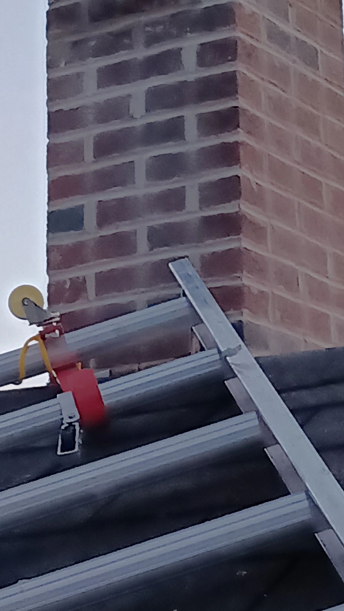 A metal ladder leaning against a roof near a brick chimney.