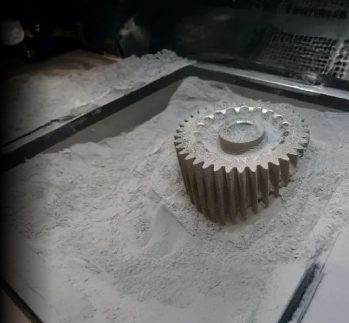A gear partially covered in white powder lies in a dust-filled container.