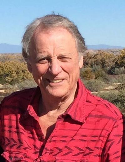 Smiling man outdoors with a red patterned shirt and natural background.