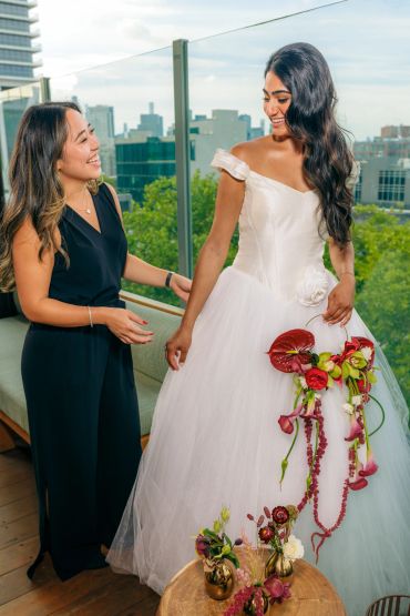 Bride in white gown and friend smiling on balcony.
