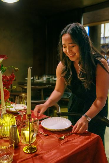 Woman setting a warmly lit dining table with a smile.