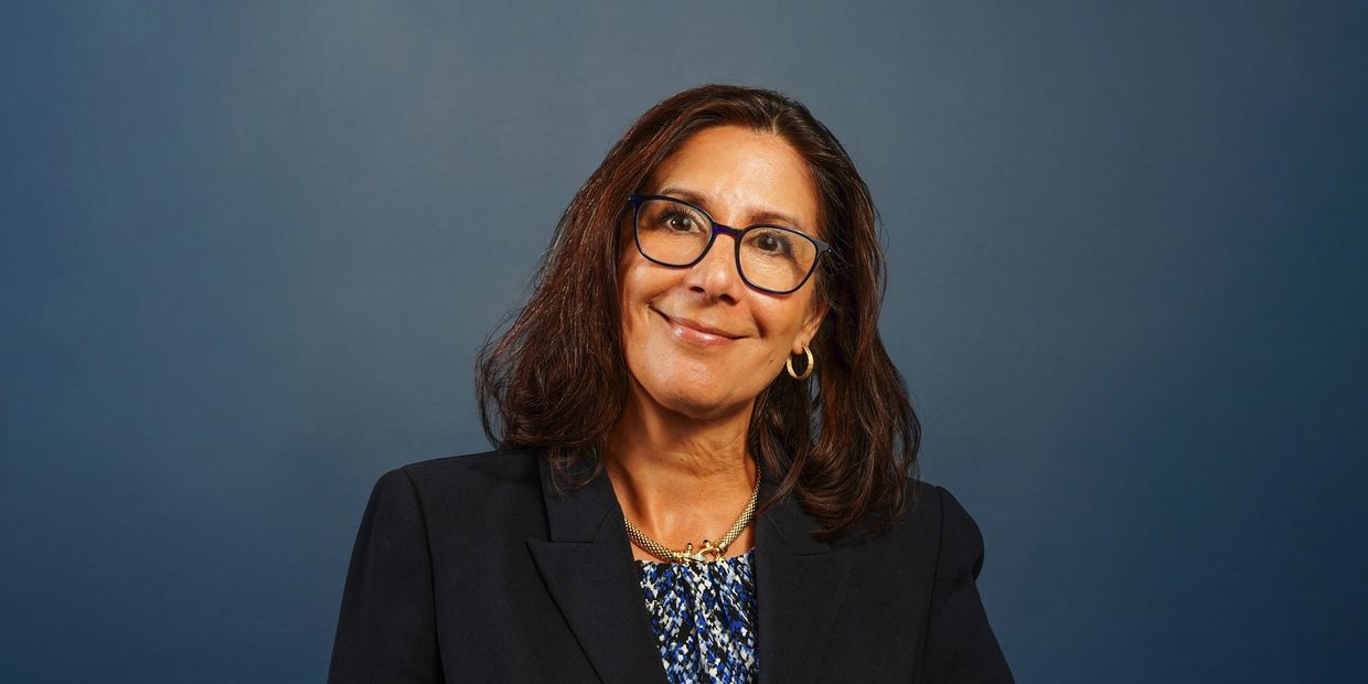 Smiling woman with glasses in professional attire against a blue background.