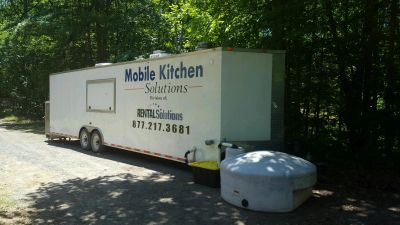 A Mobile Kitchen Solutions trailer parked by a wooded area.