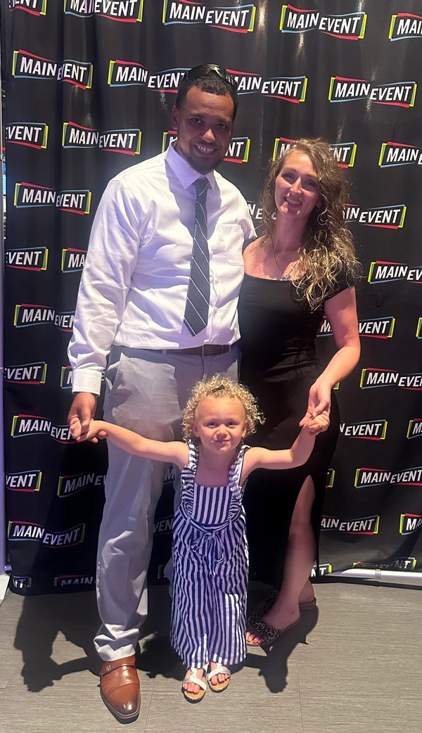 A well-dressed family posing joyfully in front of a Main Event backdrop.