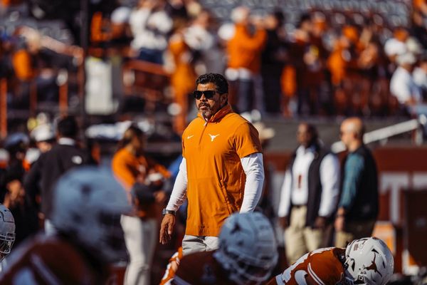 Football coach in orange gear observing players on the field.