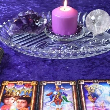 Purple candle, crystals, and tarot cards on a purple cloth.
