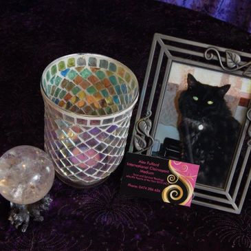 Decorative candle holder, crystal ball, and framed photo of a black cat on a dark surface.
