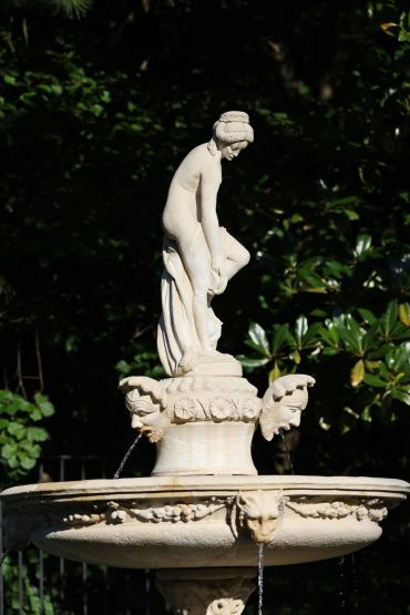 Elegant stone fountain with a classical statue in a garden.