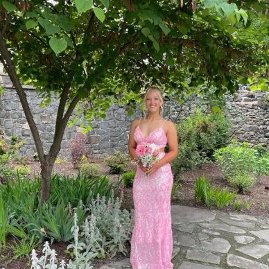 Woman in pink dress holding flowers under a tree.