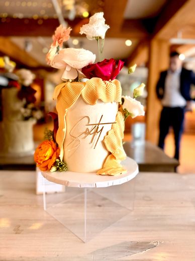 Elegant cake with flowers and signature design on a stand.
