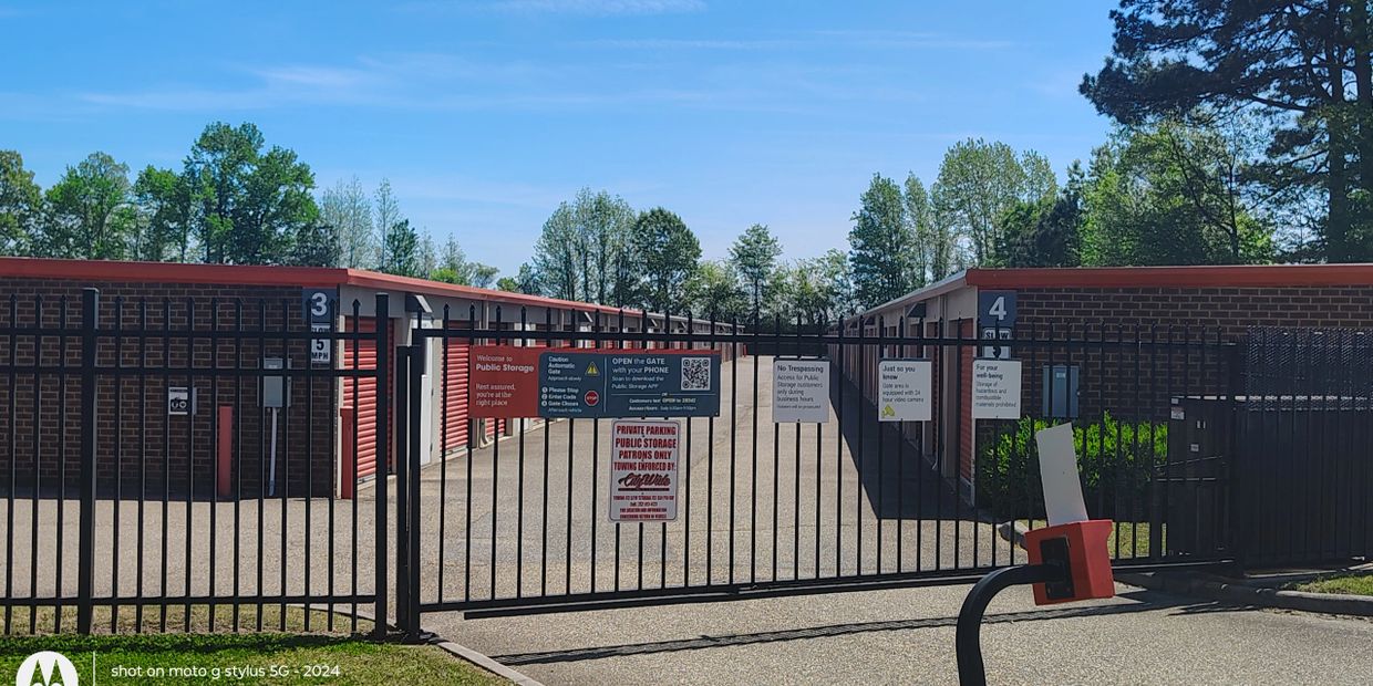 Gated public storage facility with red doors and clear signage under a blue sky.