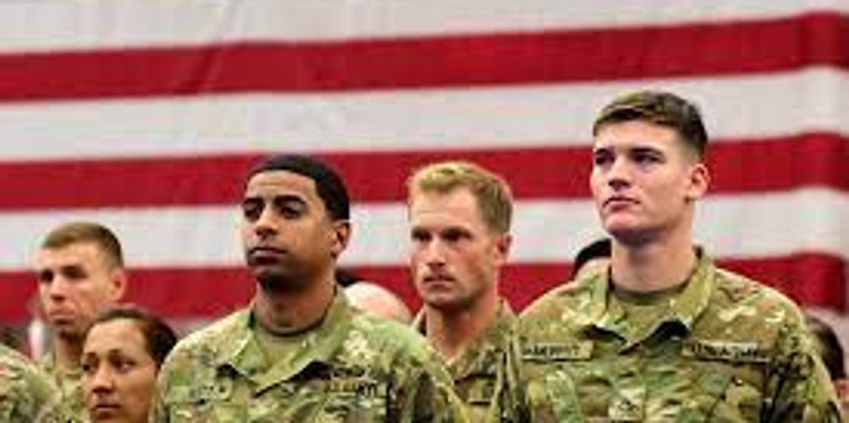 young military servicemembers standing under a flag.