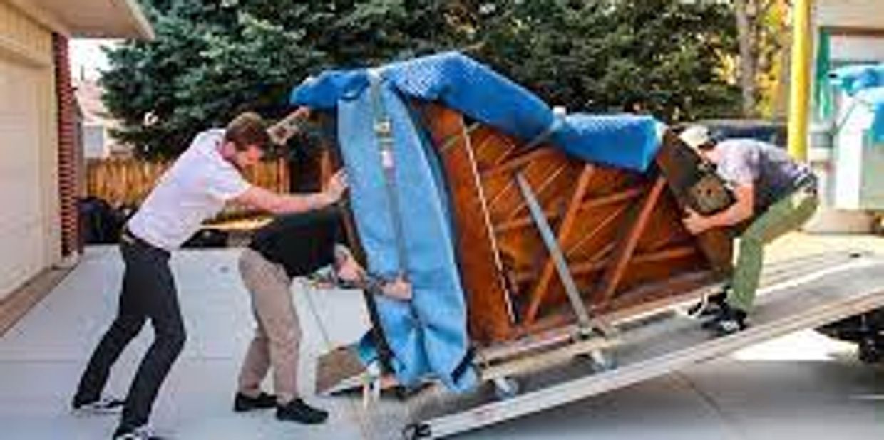 Three Movers pushing a piano up a moving truck ramp.