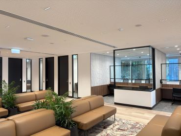 Modern office lounge with beige sofas and plants.