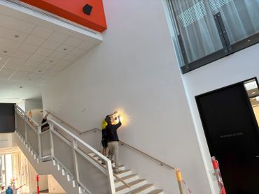 Two people on a stairway inspecting a wall with a flashlight.