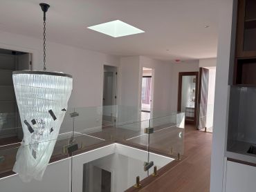 Modern stairwell with glass railing and chandelier.