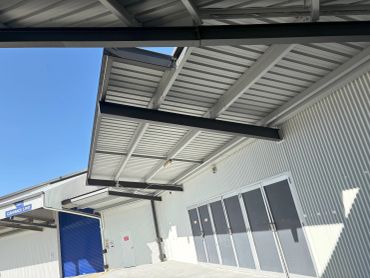 Outdoor loading area with white metal building and blue sky.
