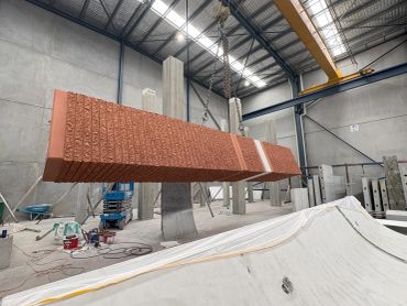 Large textured brick panel suspended in an industrial warehouse.