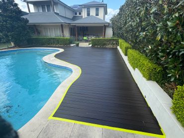 Curved swimming pool with dark wooden deck and green hedges.