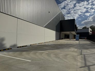 Empty industrial parking lot next to silvery metal and black buildings.