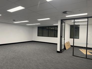 Empty modern office room with glass partition and ceiling lights.