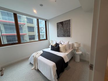 Minimalist bedroom with geometric artwork and large window.