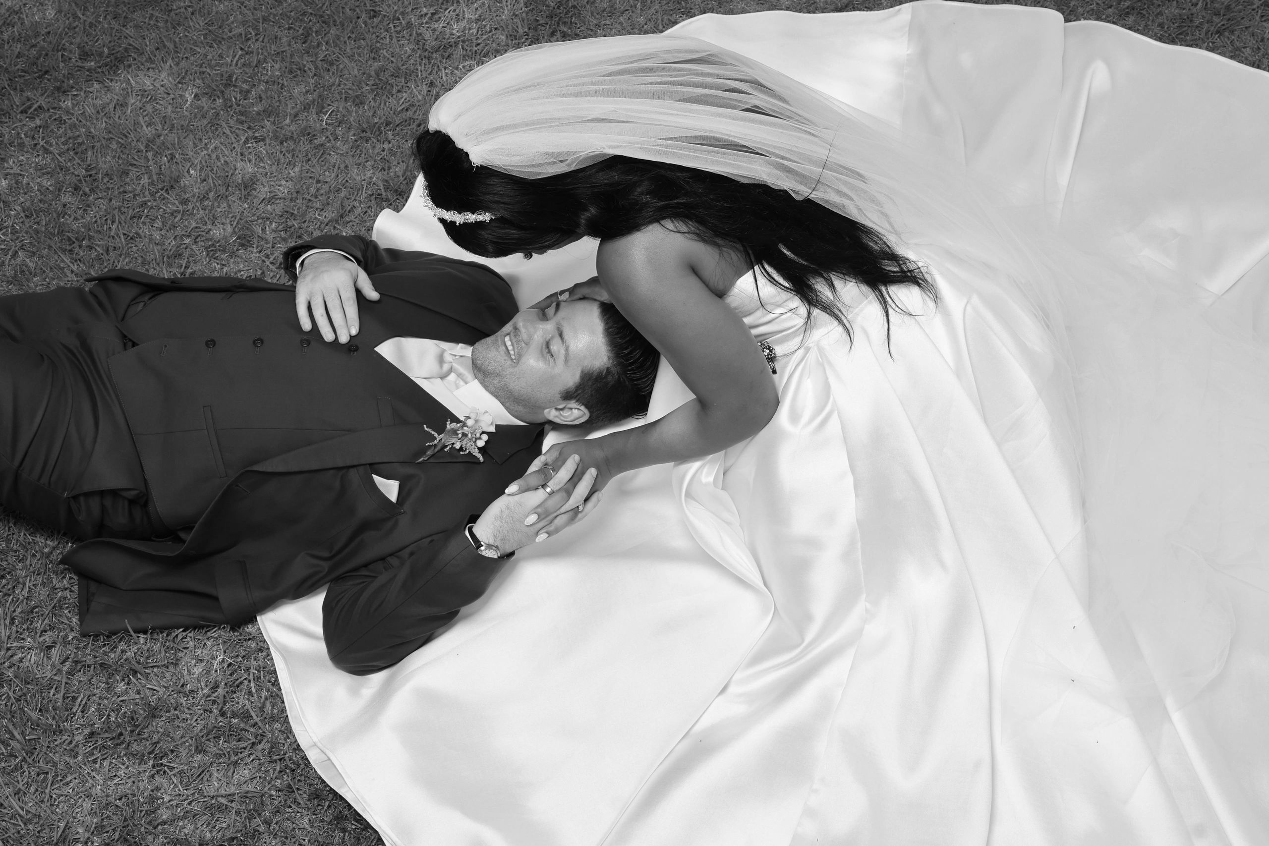Bride and groom lying on the grass holding hands.