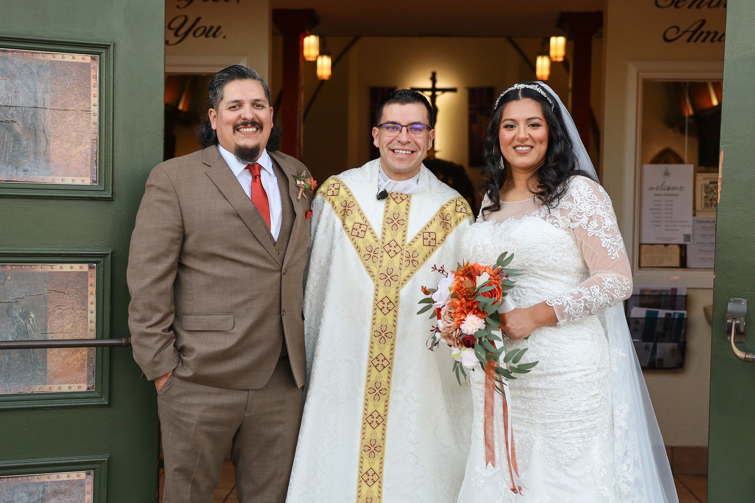 A wedding couple and priest smiling at the camera.