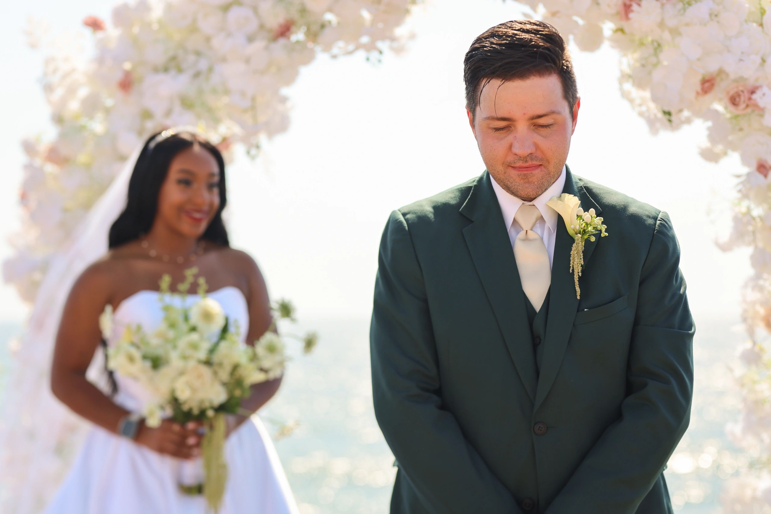 Groom anxiously waits during wedding ceremony as bride smiles behind him.