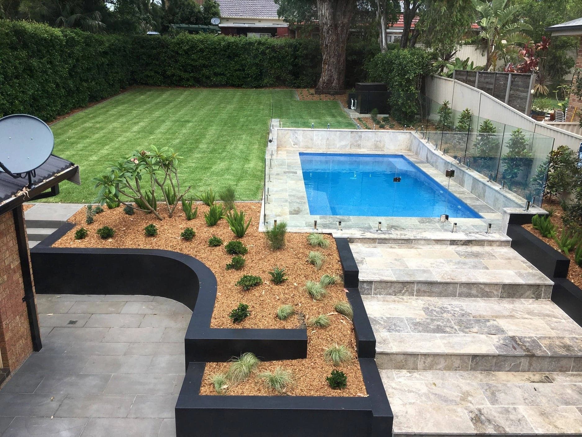 Modern backyard with a pool, lawn, and landscaped garden beds.