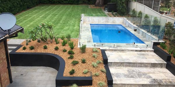 Modern backyard with a small pool, glass fence, and manicured lawn.