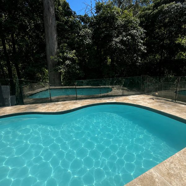 Two swimming pools surrounded by trees and a protective glass fence.