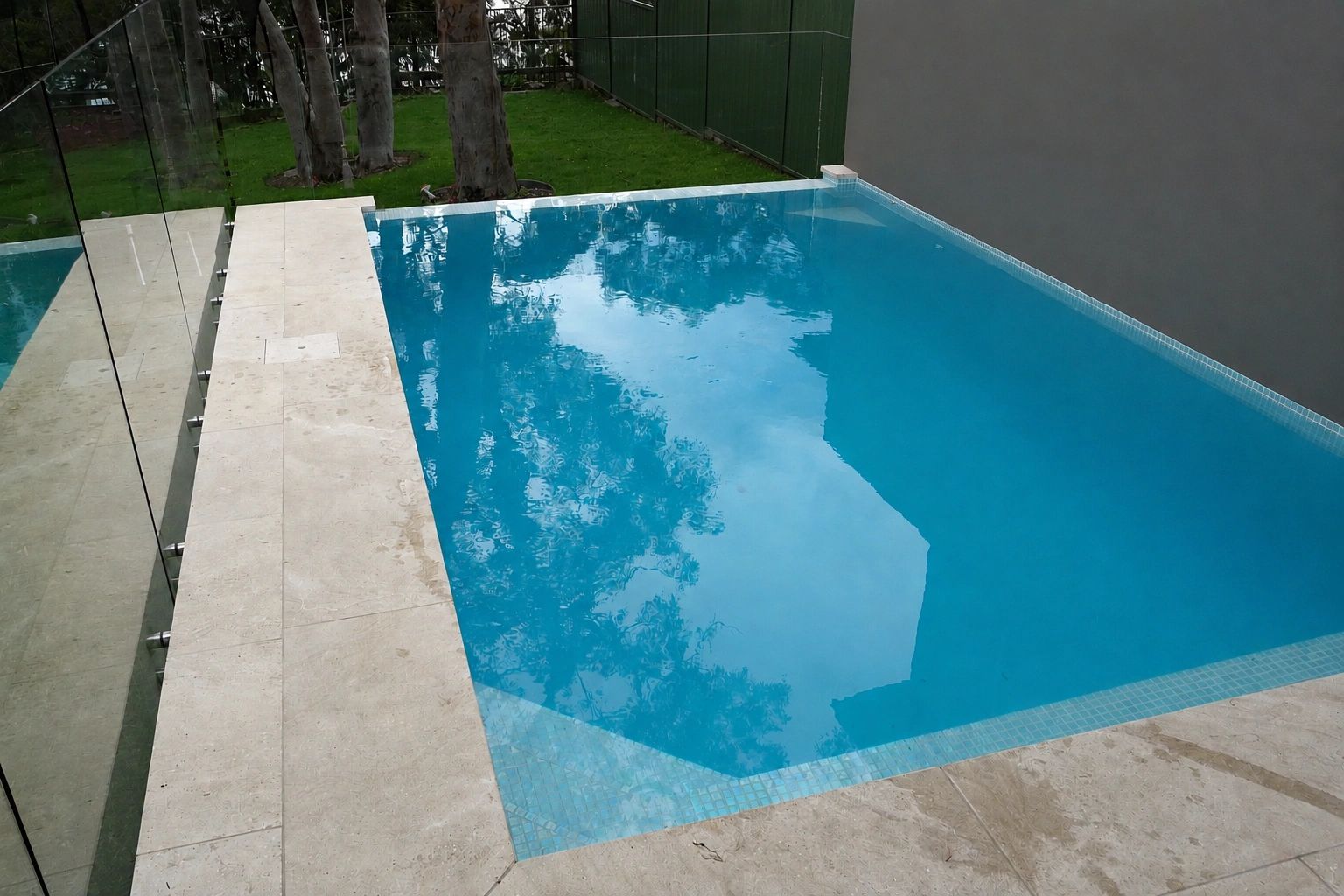 Modern private swimming pool with clear blue water and glass fencing.