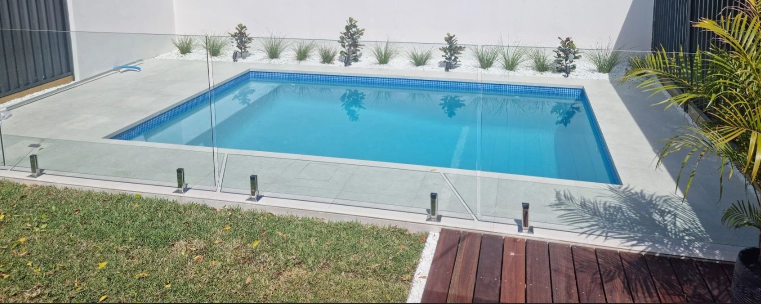 Modern backyard pool with glass fencing and greenery.
