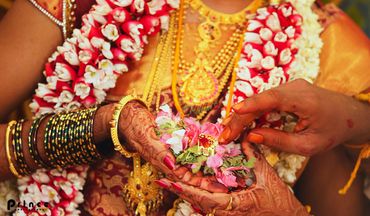Close-up of a traditional Indian wedding ritual with floral garlands and henna-adorned hands.