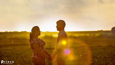 Couple holding hands, gazing at each other during golden sunset.