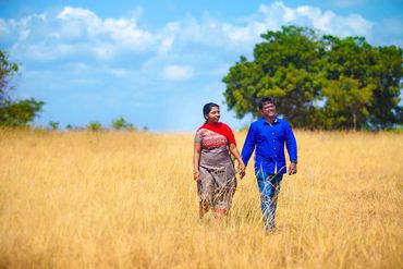 Couple walking in grassy field for pre-wedding shoot in Thanjavur by Luster Pearl Media.