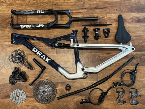 Disassembled PEAK mountain bike frame and components laid out on wooden floor.